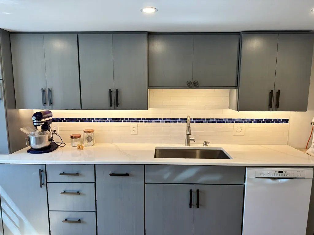 Gray kitchen cabinets with a white countertop, backsplash, and appliances.