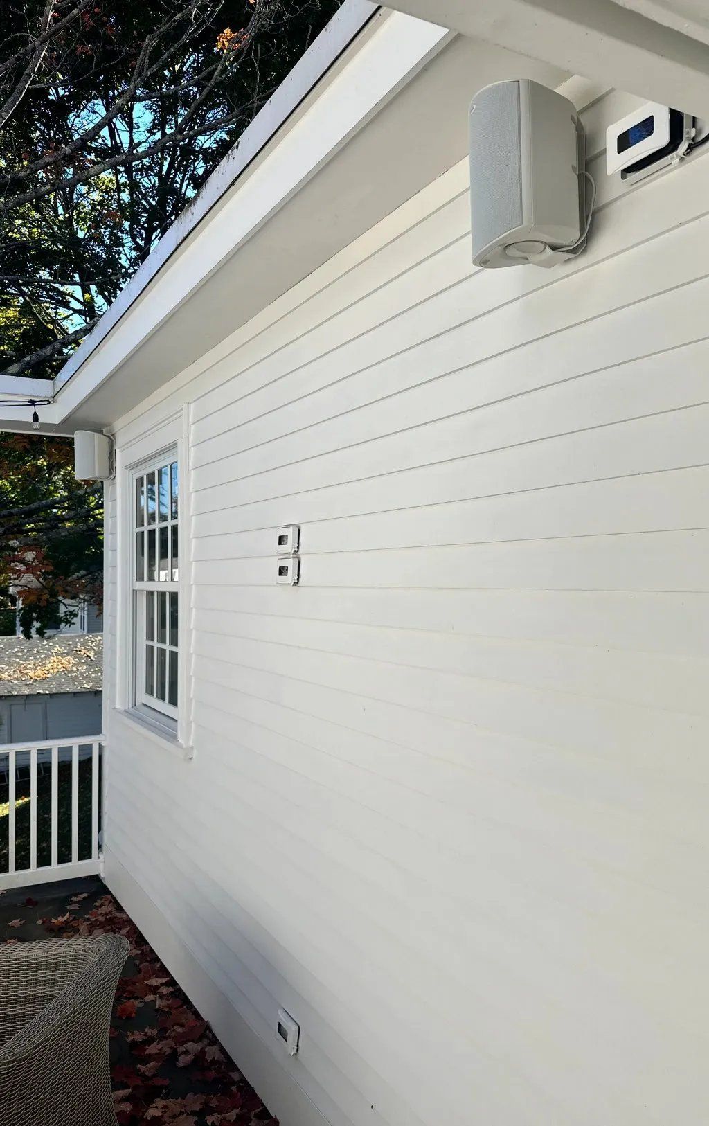White building exterior with a window, speakers, and an outdoor light.