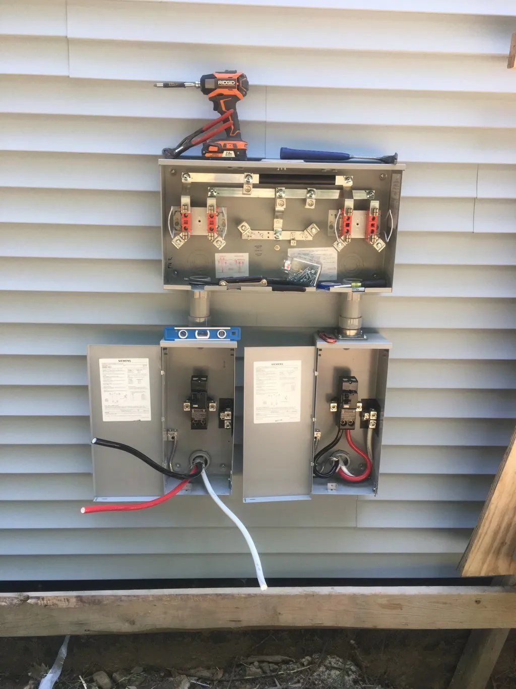 Electrical junction boxes mounted on siding; a drill rests on the top box.