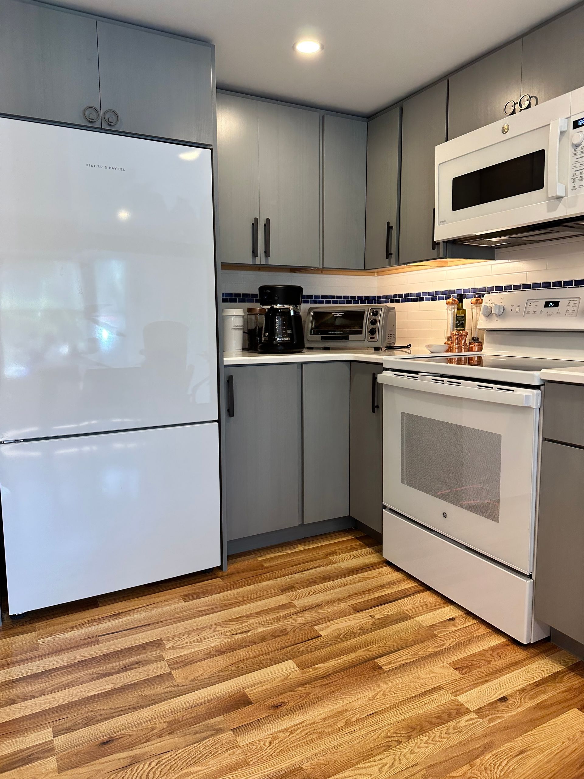 Kitchen with white appliances, gray cabinets, wood floor, and overhead lighting.