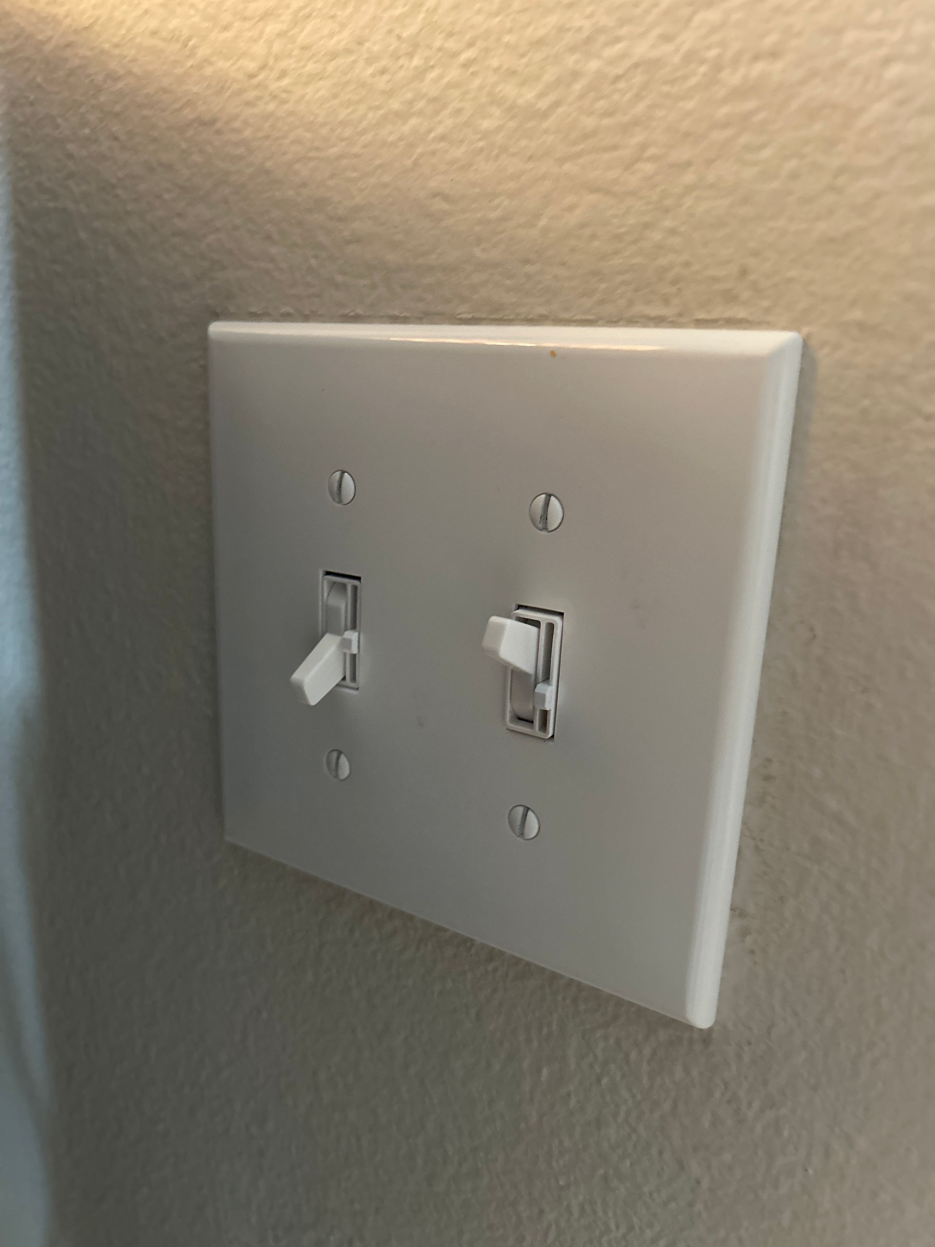A white electrical switch plate with two toggle switches on a beige wall.