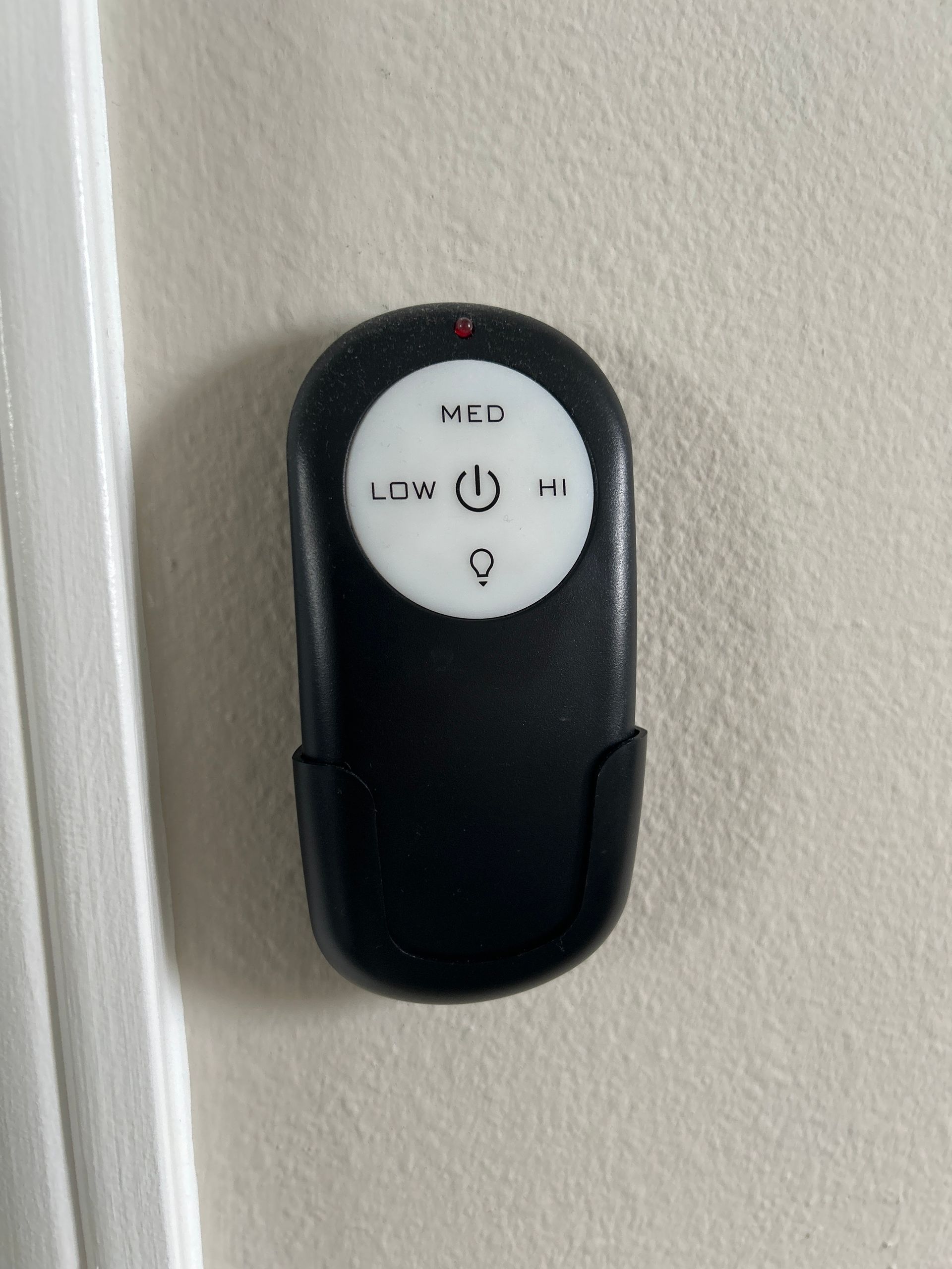 Black ceiling fan remote mounted on a white wall, with buttons for light and fan speeds.