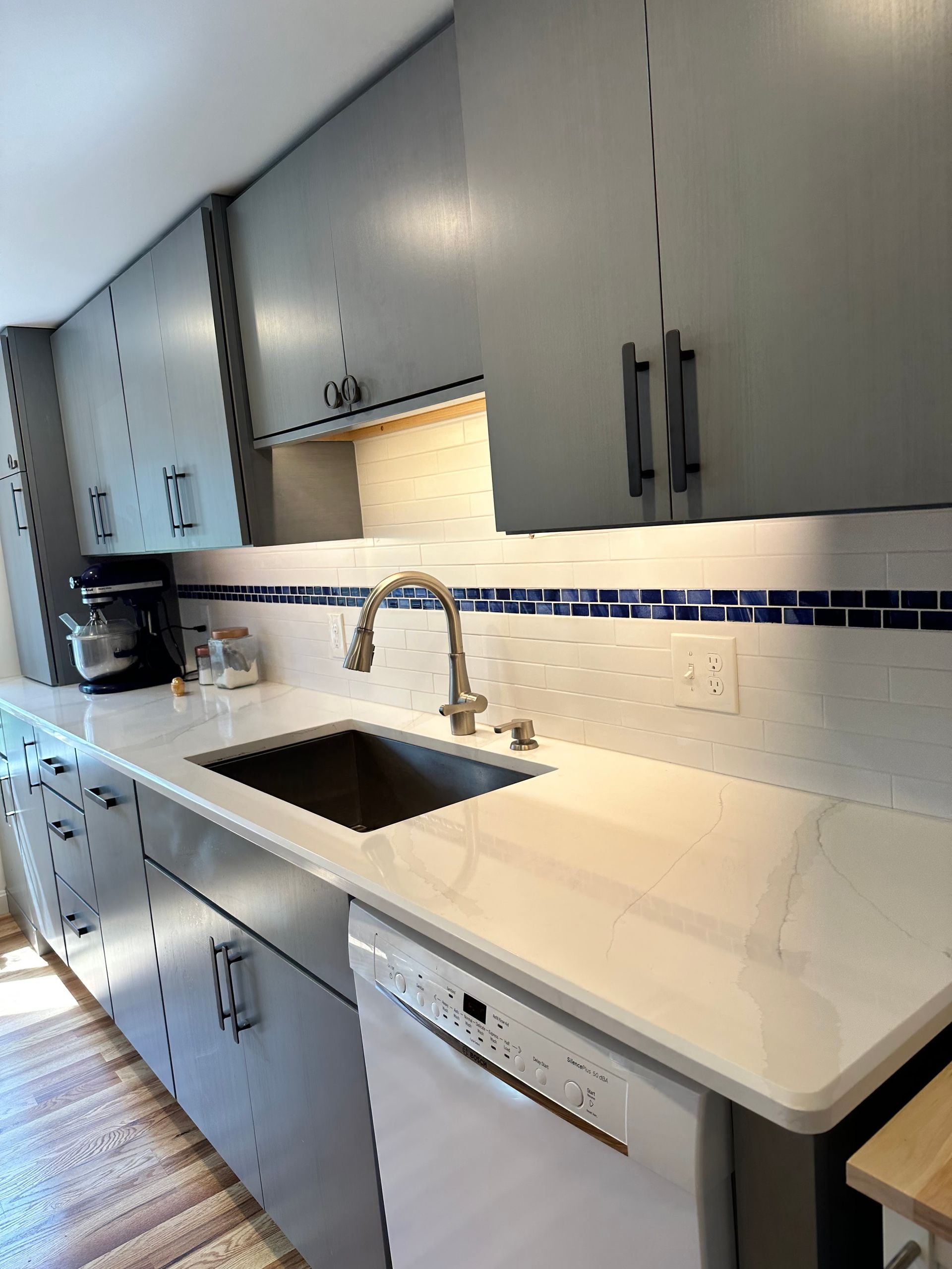Gray kitchen cabinets with a white countertop and stainless steel sink and appliances.
