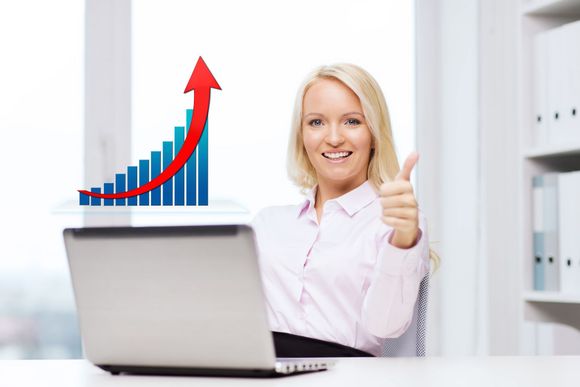 A woman is sitting at a desk with a laptop and giving a thumbs up.