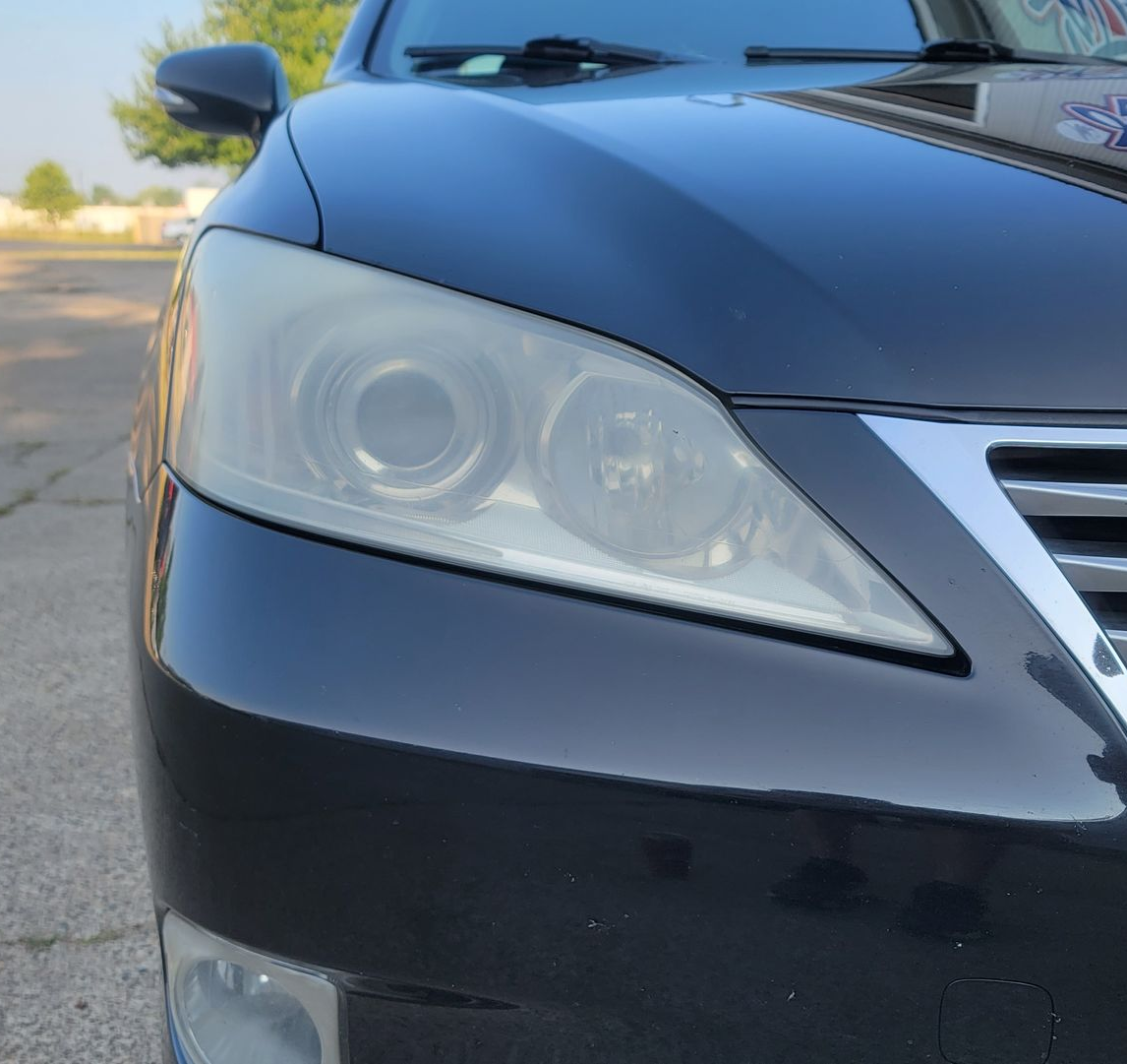 Black car with headlights open, being worked on. Tools, tape, and pads are visible.