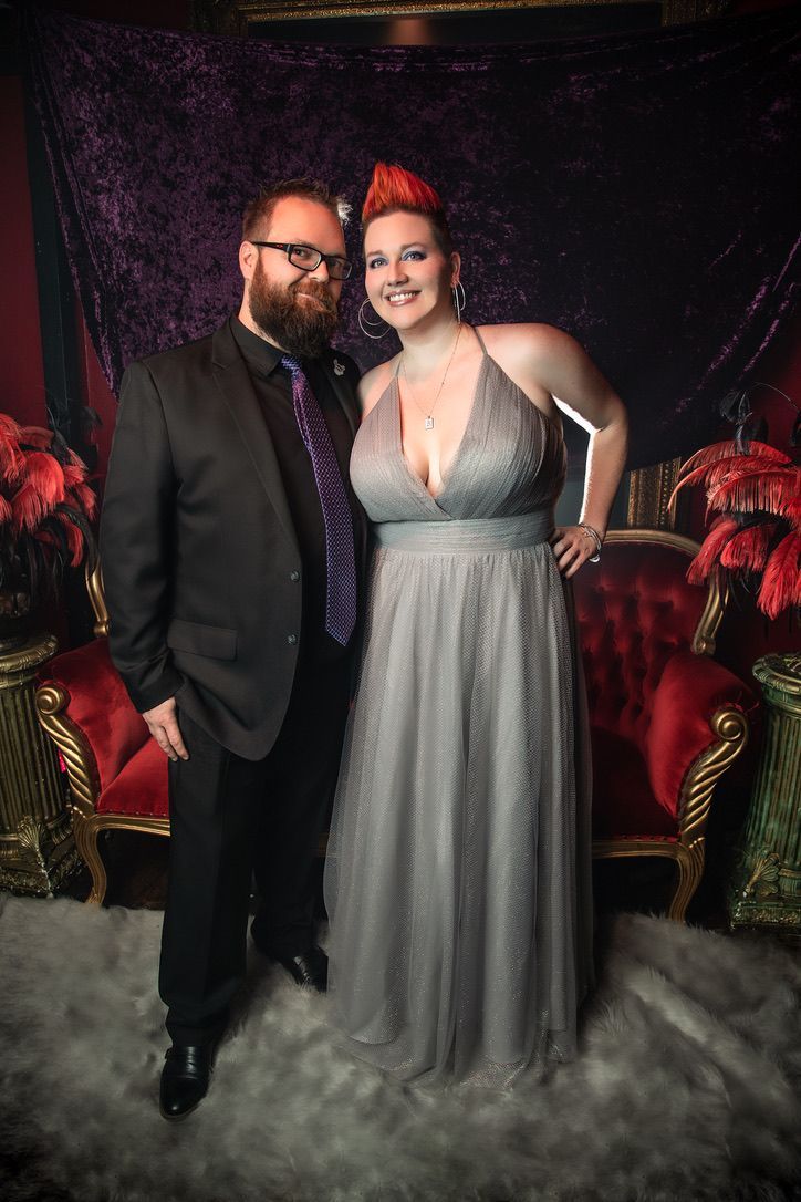 A man and a woman are standing next to each other in front of a red chair.