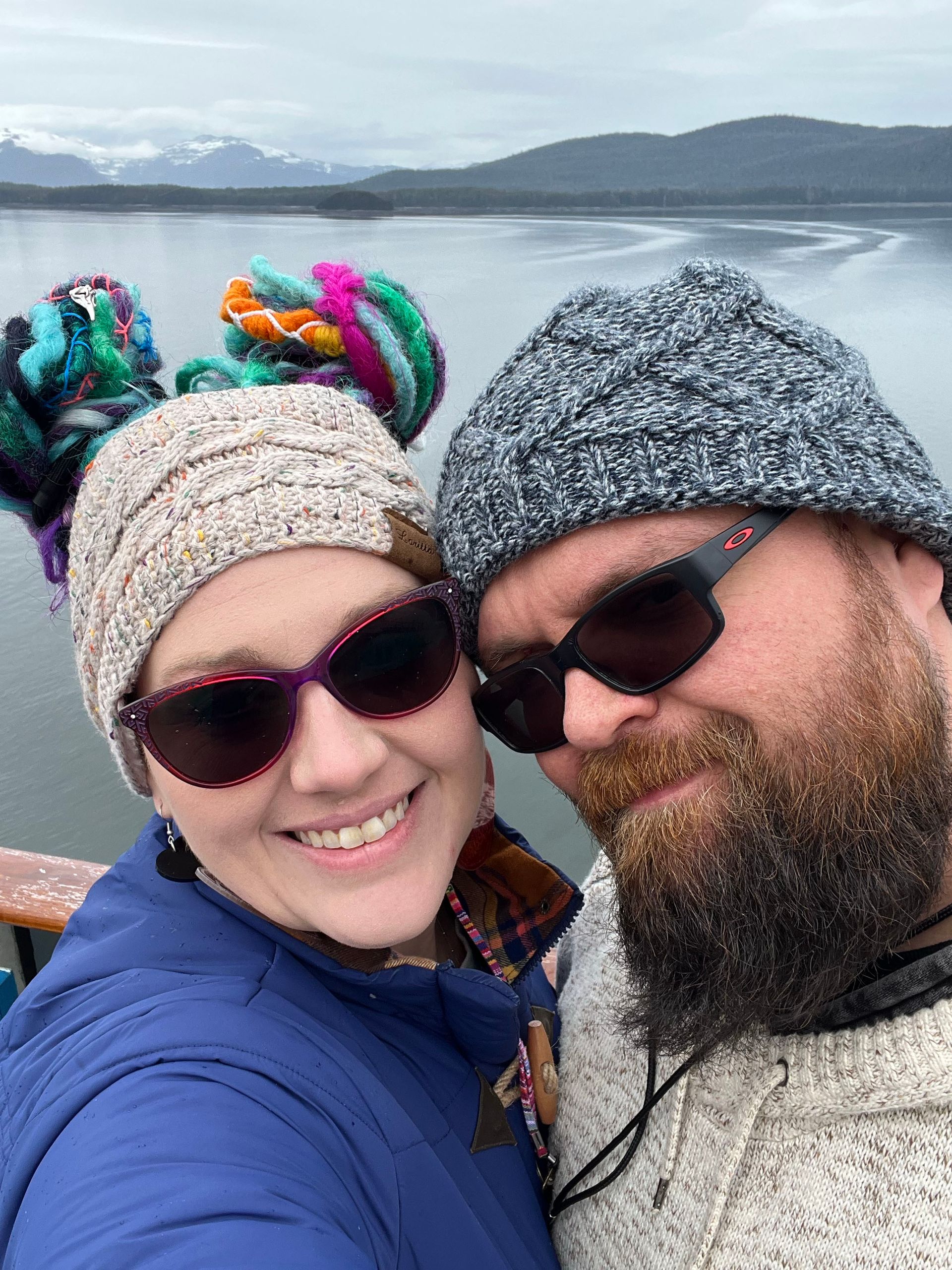 A man and a woman are posing for a picture in front of a lake.