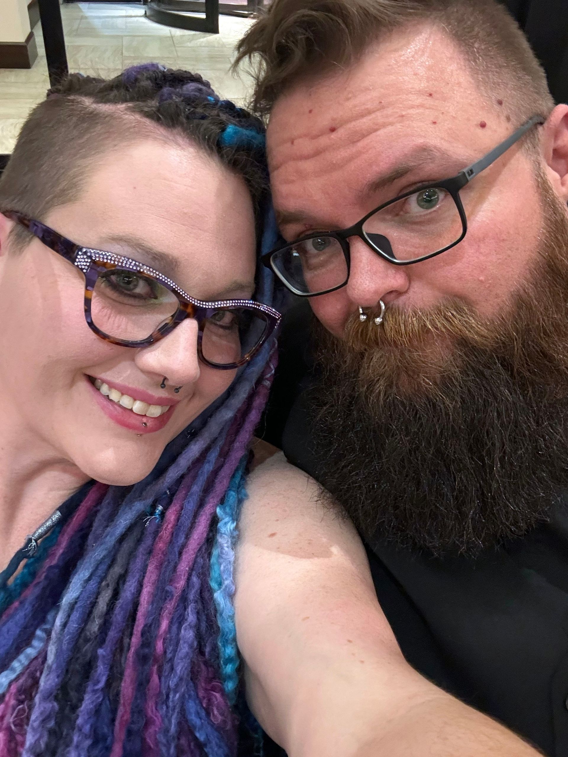 A man with a beard and a woman with dreadlocks are posing for a picture.