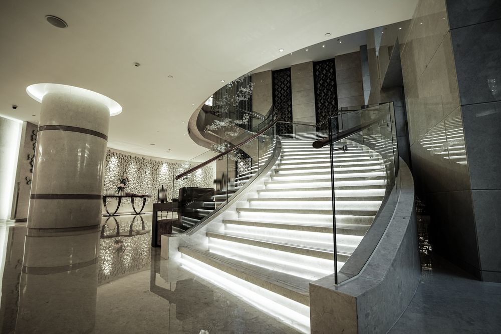 A Large Curved Staircase With a Glass Railing in a Lobby — Paul Cooper Homes In Noosa Heads, QLD