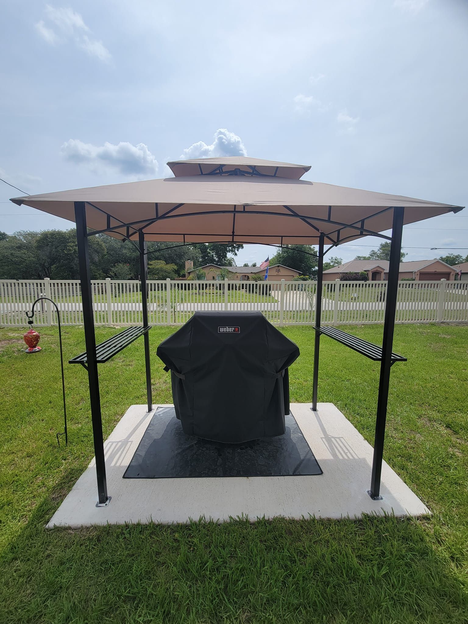A gazebo with a grill underneath it in a backyard.