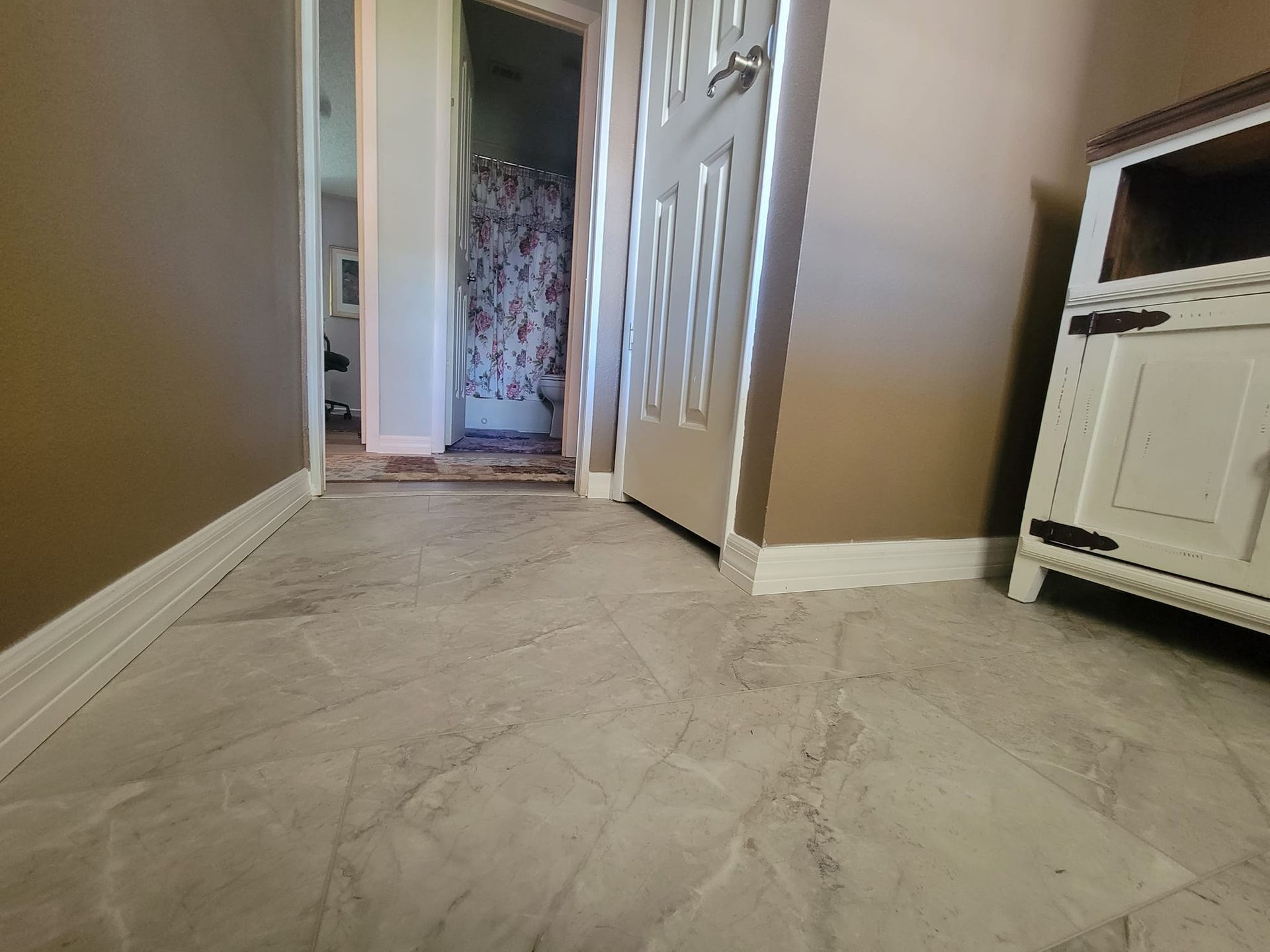 A hallway with a tiled floor and a door leading to a bathroom.
