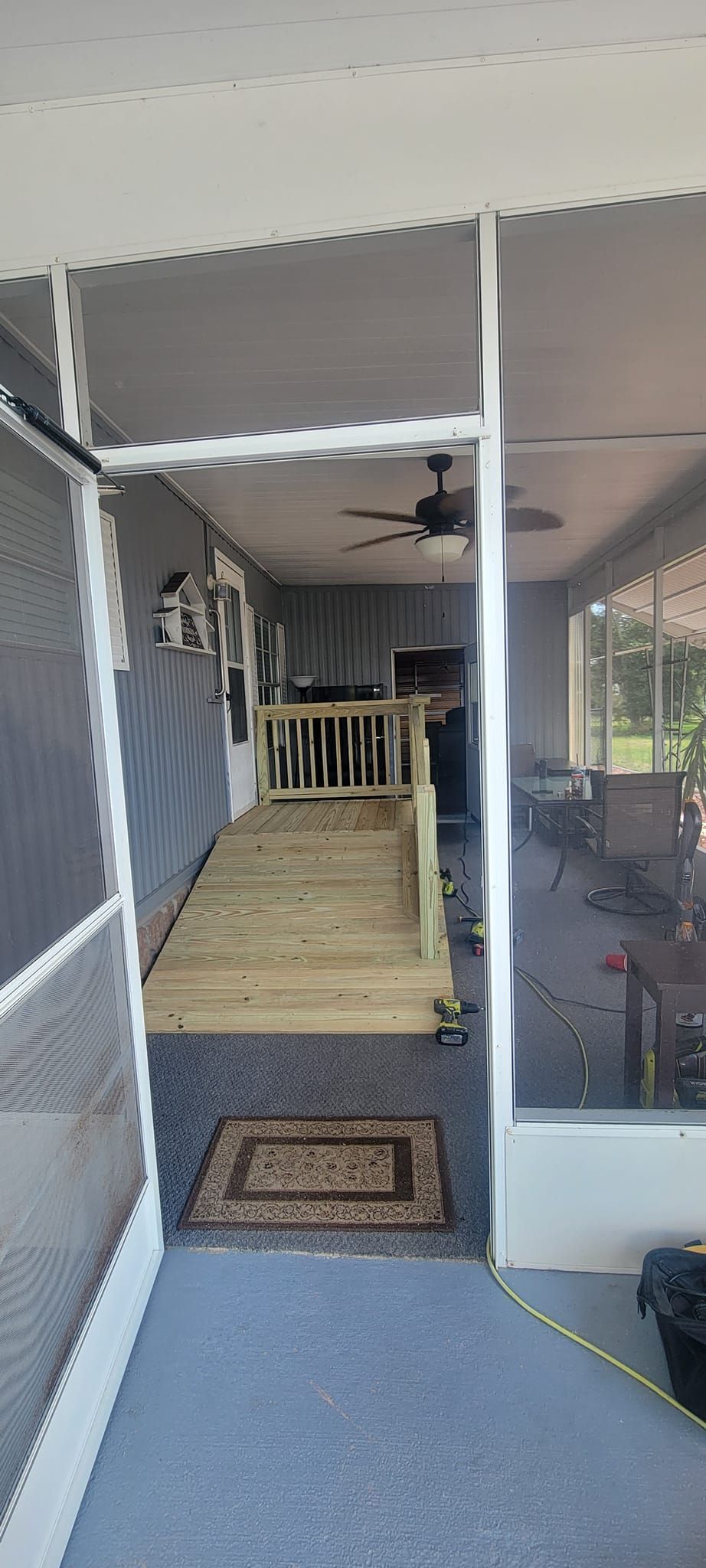 A screened in porch with a wooden ramp and a ceiling fan.