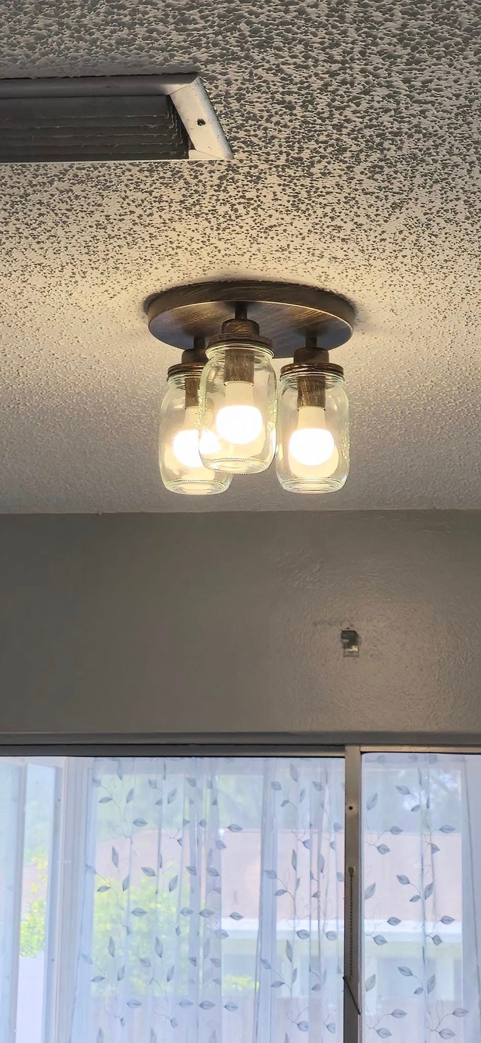 A ceiling light with mason jars on it is hanging from the ceiling in a room.