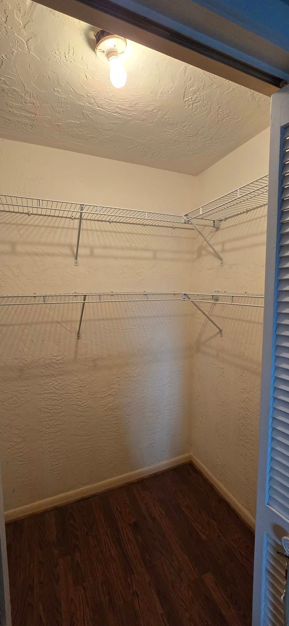 An empty walk in closet with wooden floors and a light on the ceiling.