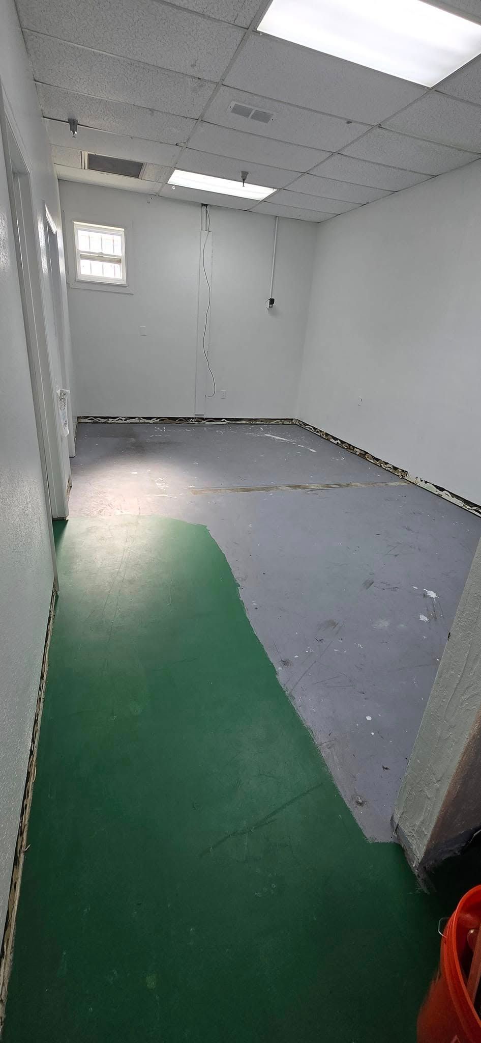 A long hallway with a green carpet and a bucket on the floor.