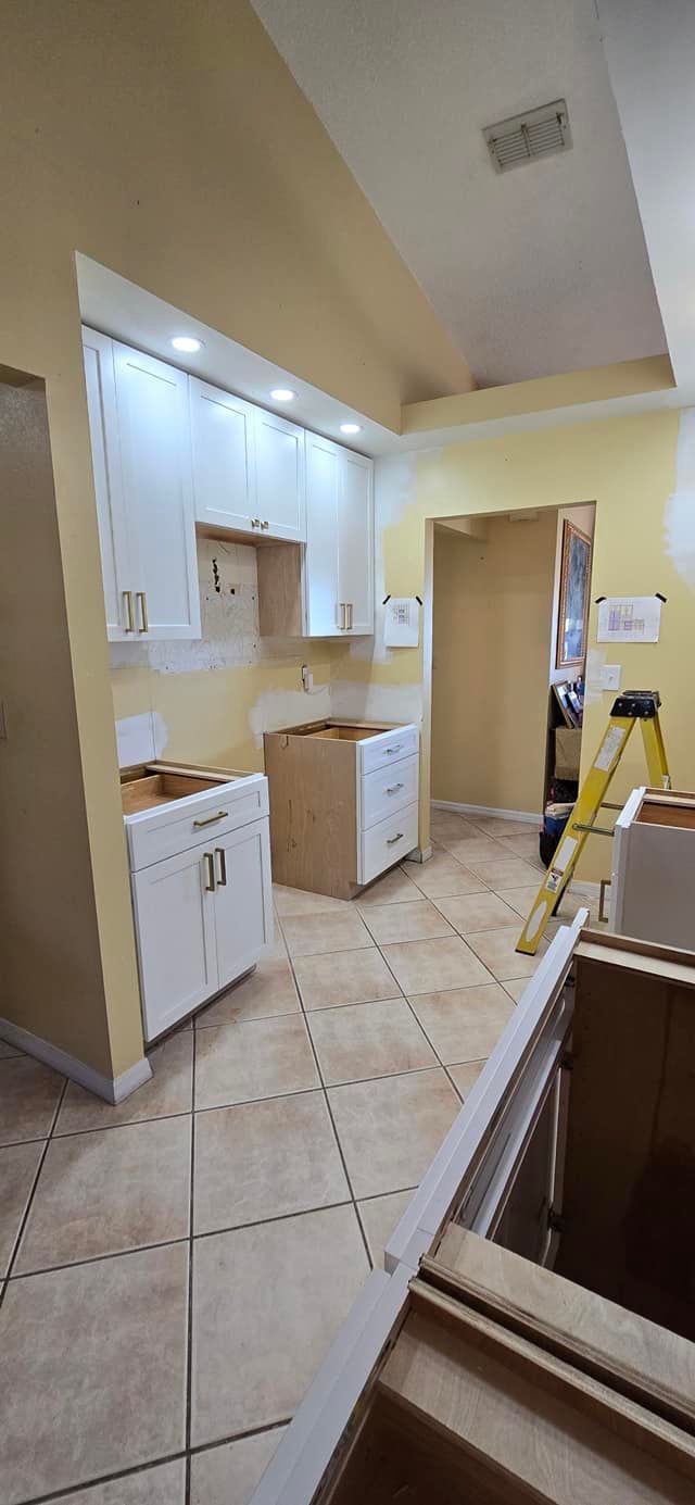 A kitchen under construction with white cabinets and a yellow ladder.