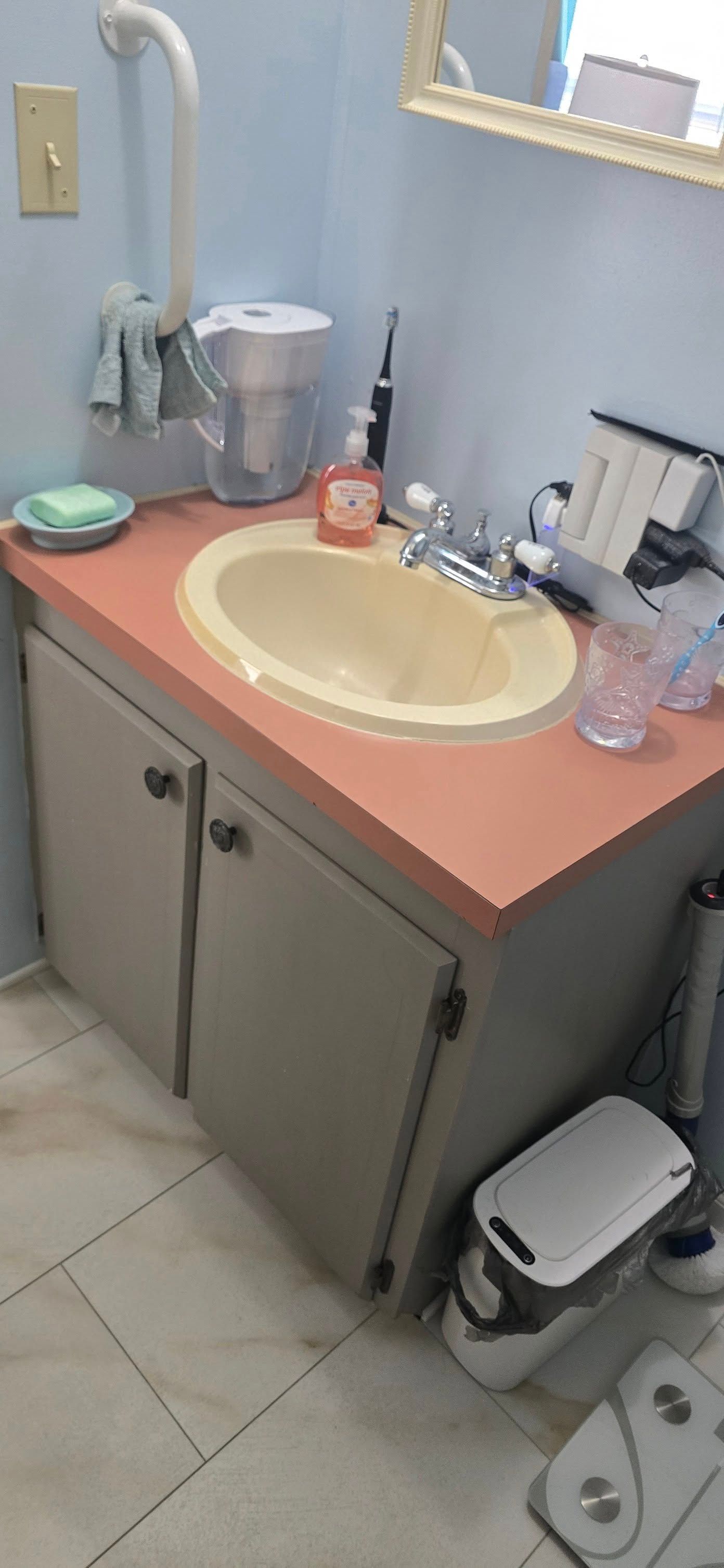 A bathroom with a sink , toilet , trash can and mirror.