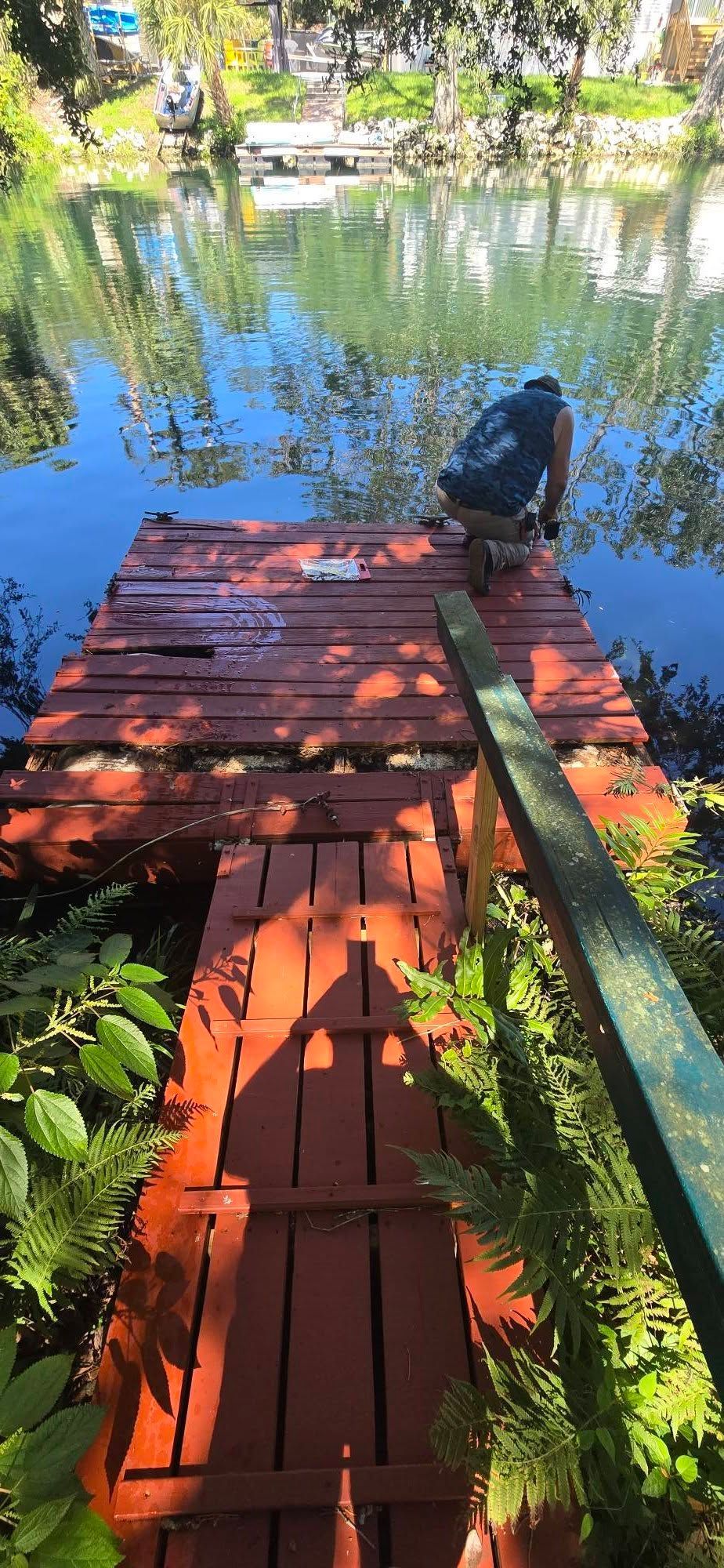 A man is working on a wooden dock next to a lake.