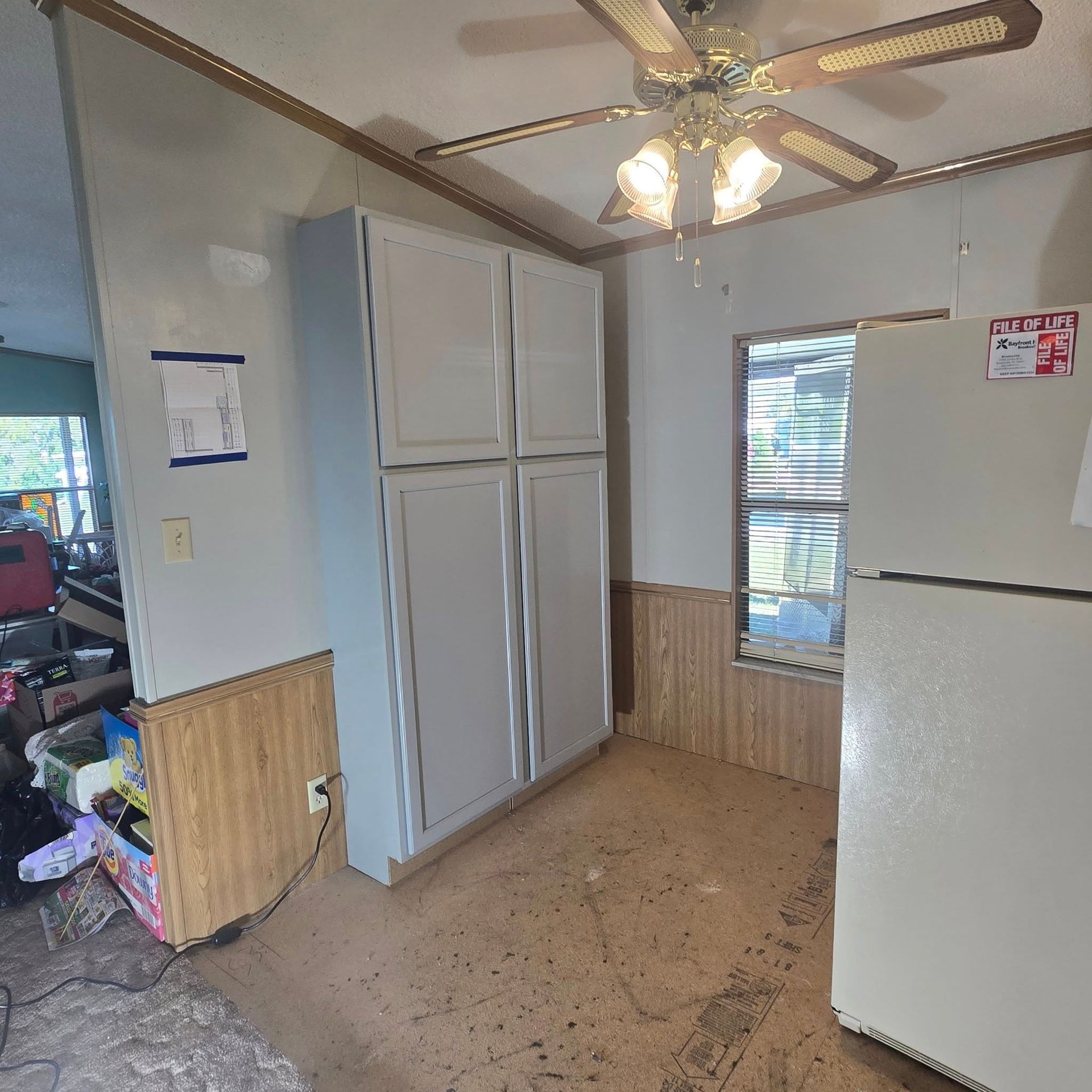 A kitchen with a refrigerator , cabinets , and a ceiling fan.