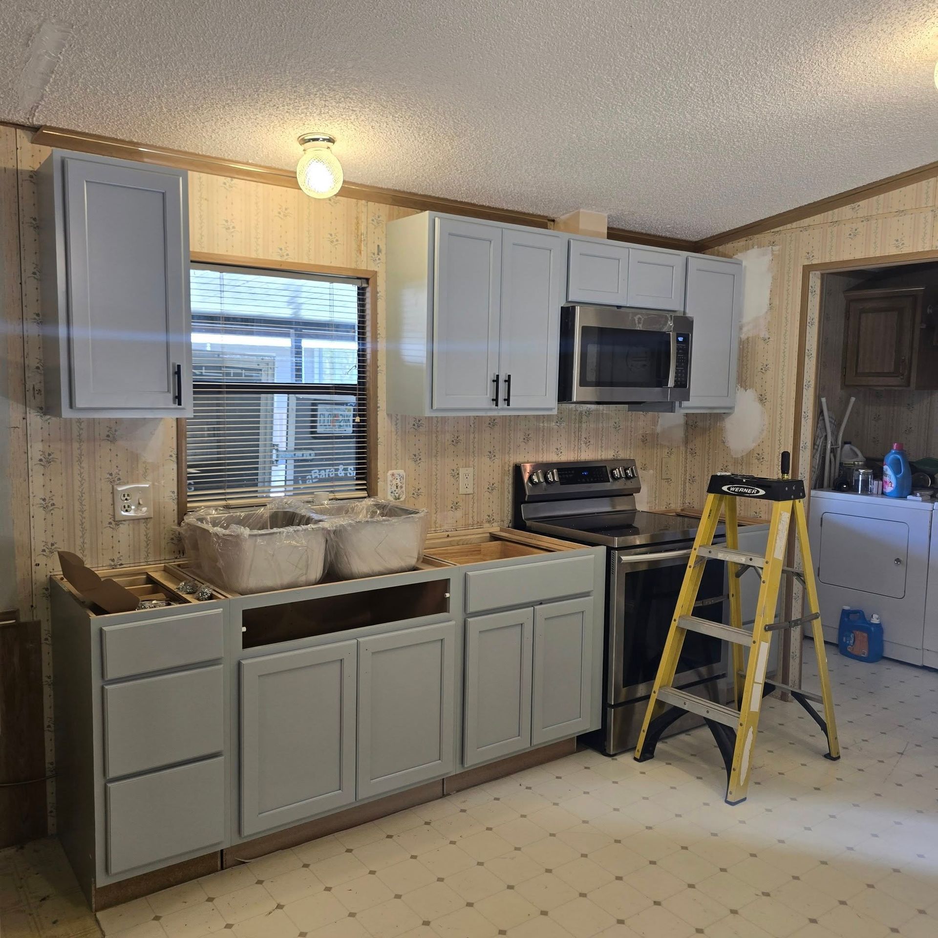 A kitchen with gray cabinets , a yellow ladder , a stove and a microwave.