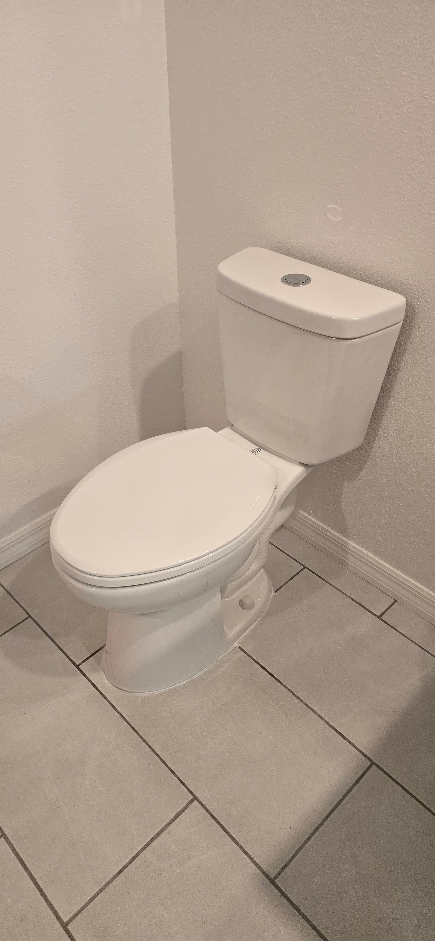 A white toilet is sitting on a tiled floor in a bathroom.