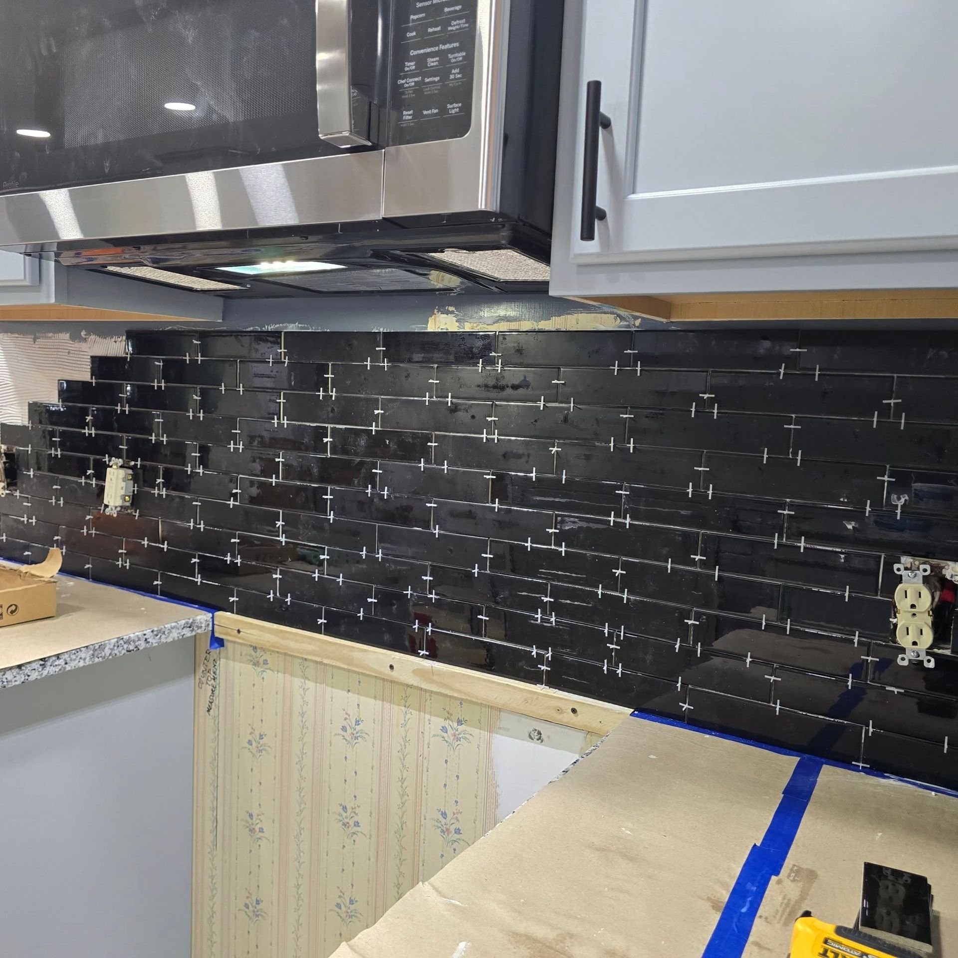A kitchen with black tiles and a stainless steel microwave