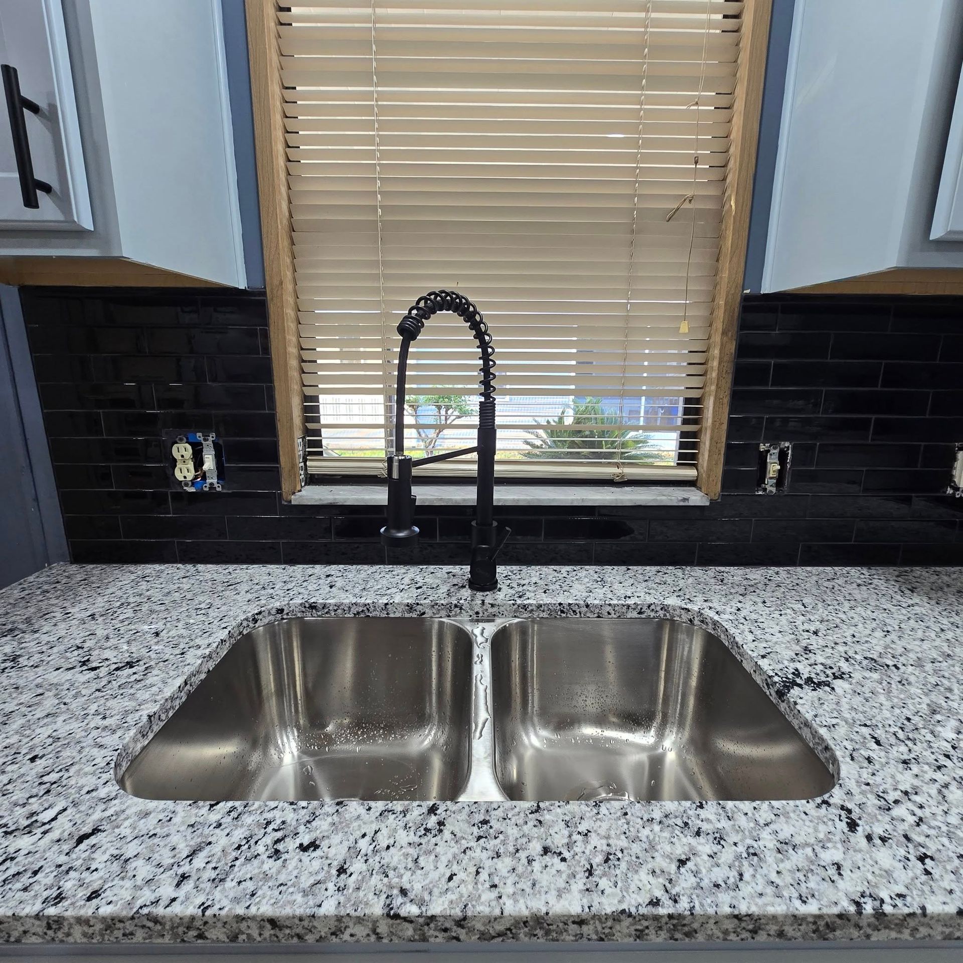 A kitchen sink with a faucet and a window with blinds.