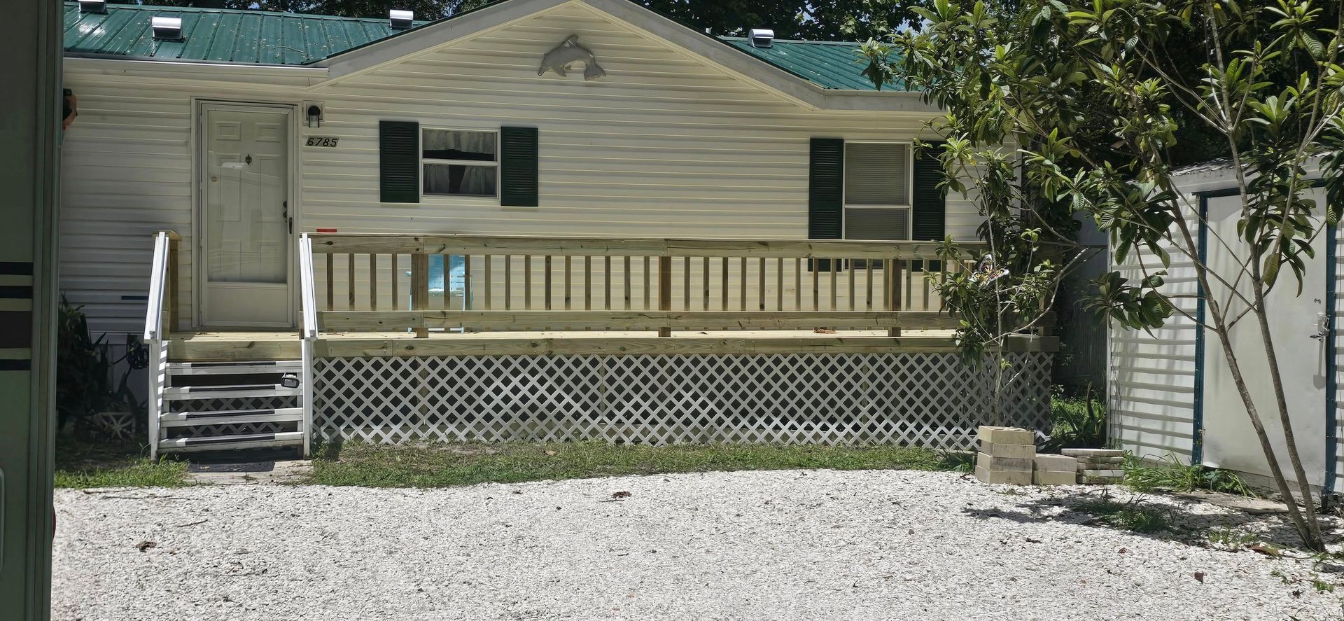 A mobile home with a green roof sits in a gravel lot