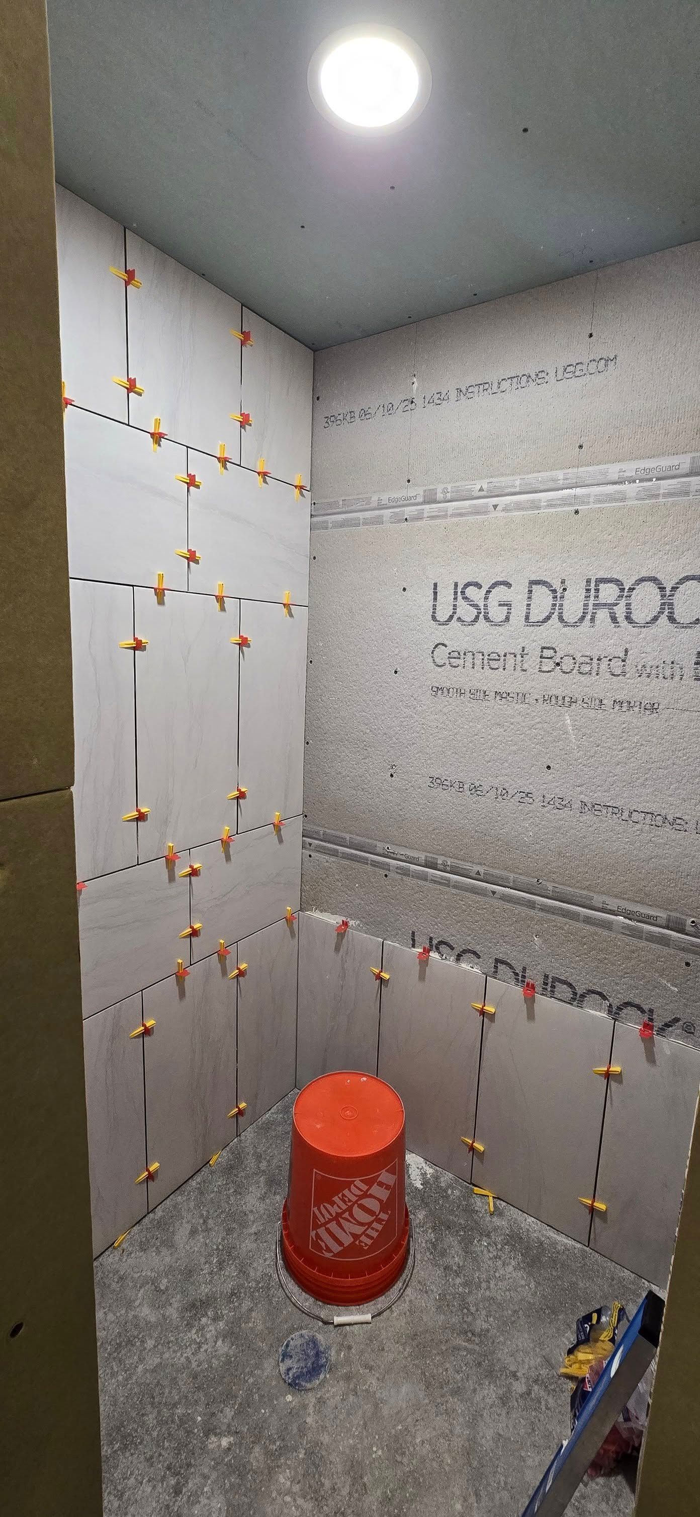 A bathroom under construction with tiles on the walls and a bucket on the floor.