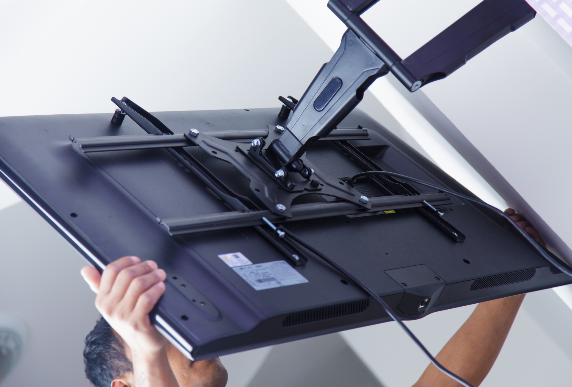 A man is hanging a flat screen tv from the ceiling