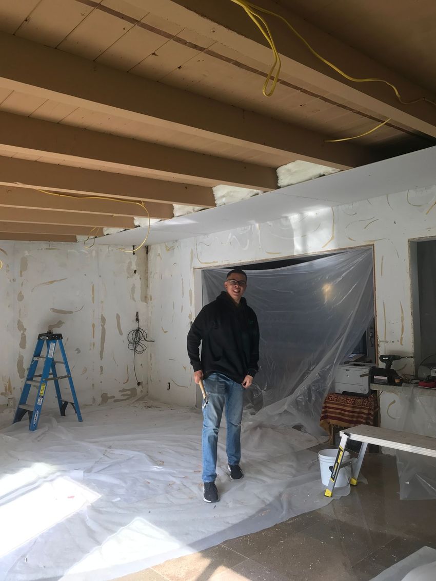 Two men are working on a wall in a room.