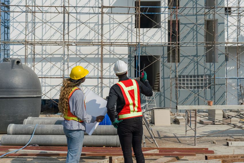 Two construction workers are standing in front of a building under construction.