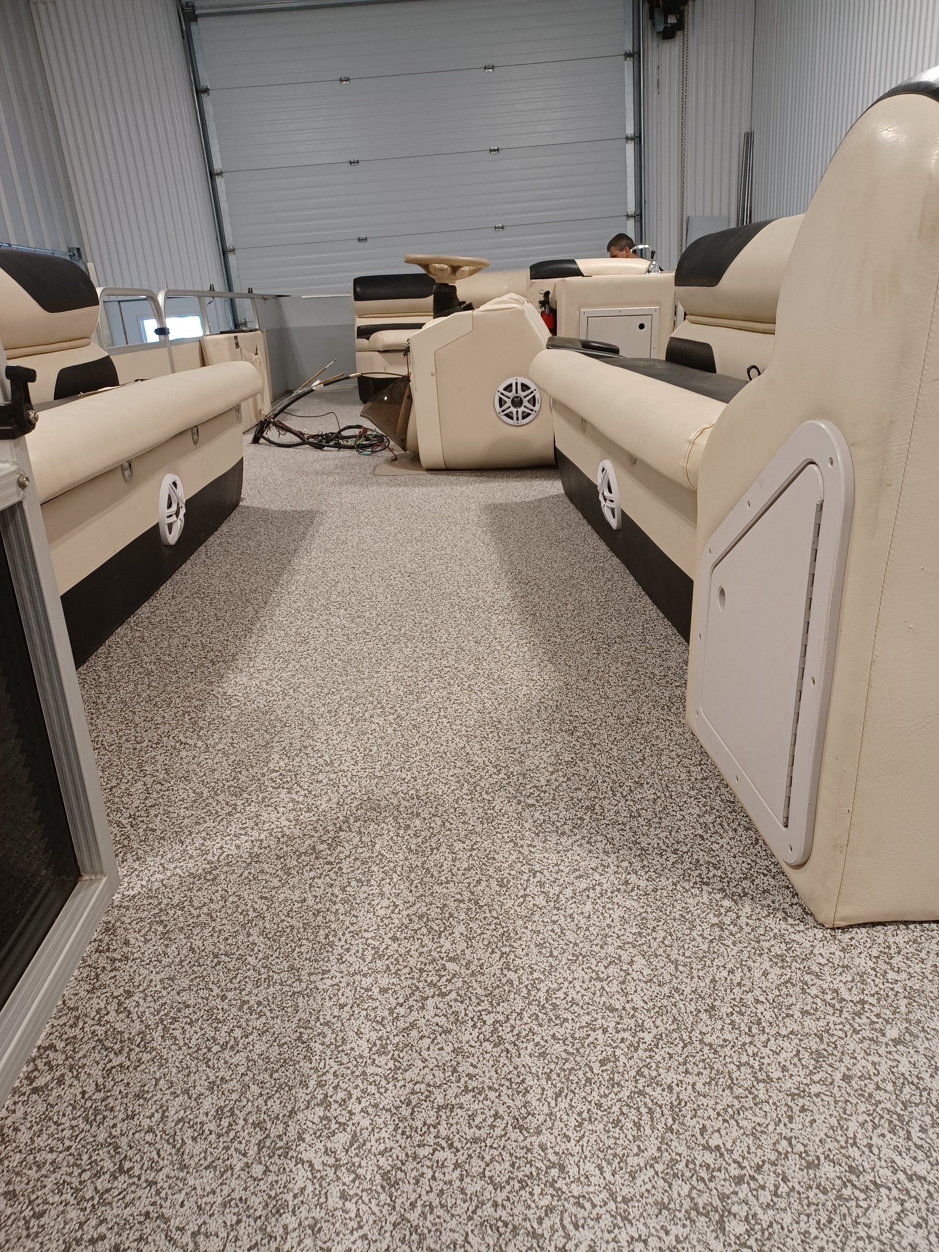 Intérieur d'un bateau ponton avec sièges beiges et plancher gris moucheté. Des compartiments de rangement sont visibles.