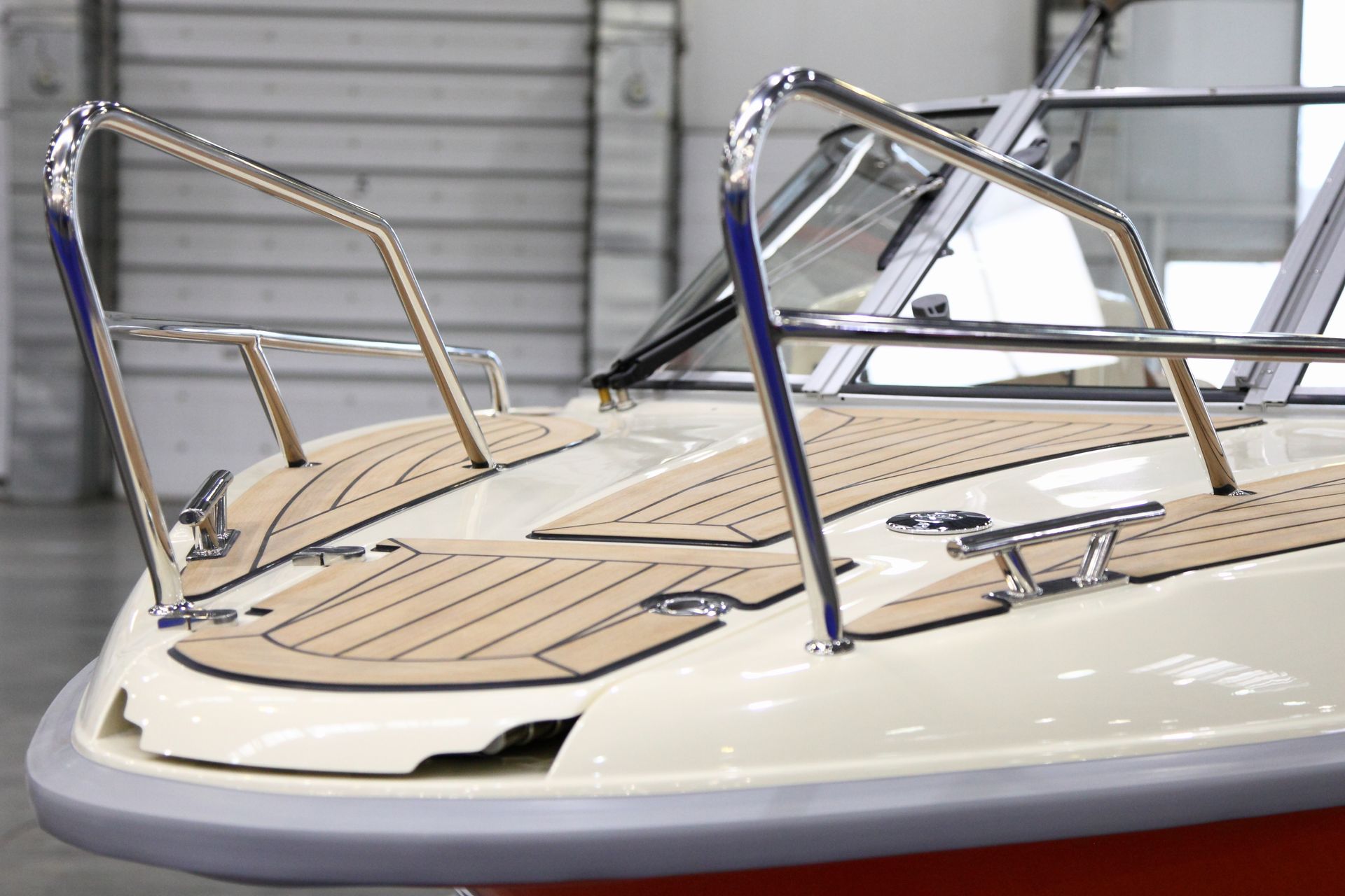 Proue d'un bateau à moteur blanc avec rambarde chromée et pont texturé beige.