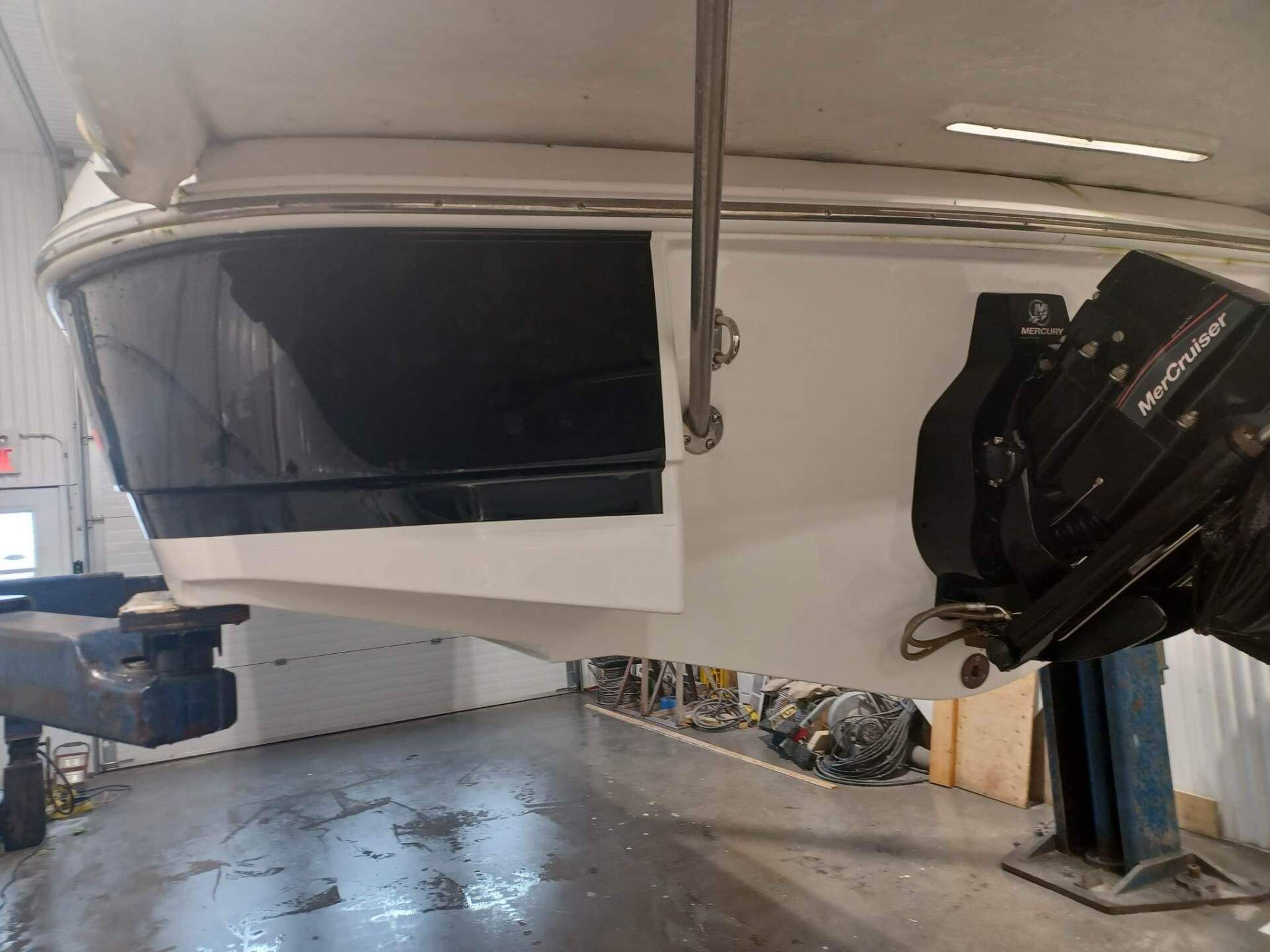 Poupe d'un bateau blanc et noir équipé d'un moteur Mercury Mercruiser, dans un bâtiment intérieur.