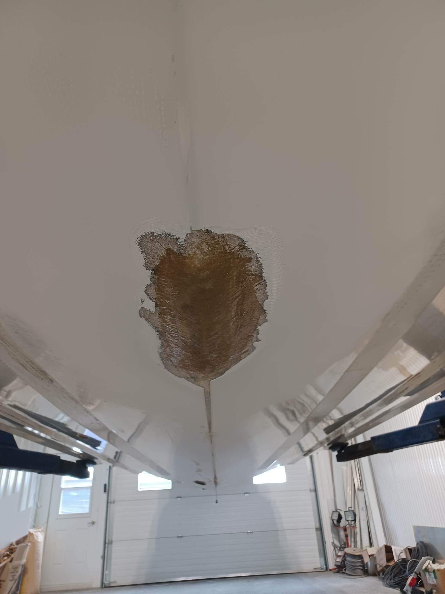 Face inférieure de la coque blanche d'un bateau, montrant une grande zone de matériau endommagé, brun et qui se détache.