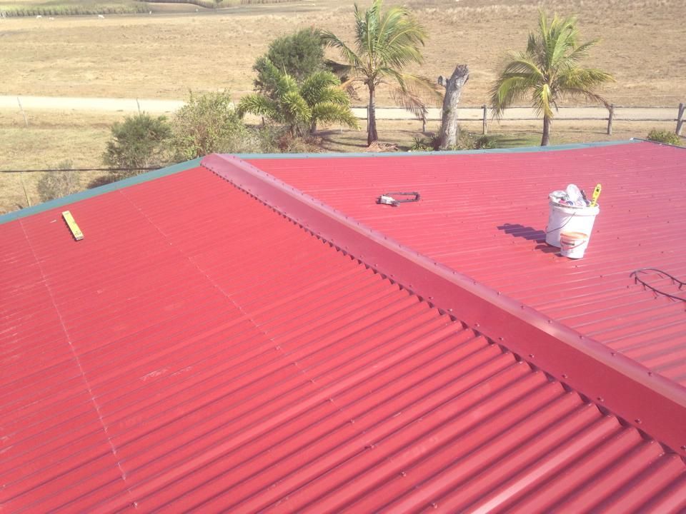 Red Corrugated Metal Roof With Tools, Palms, and Landscape — LJG Plumbing In Sarina, QLD