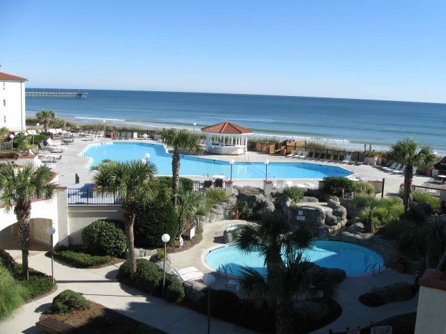 A large swimming pool surrounded by palm trees next to the ocean