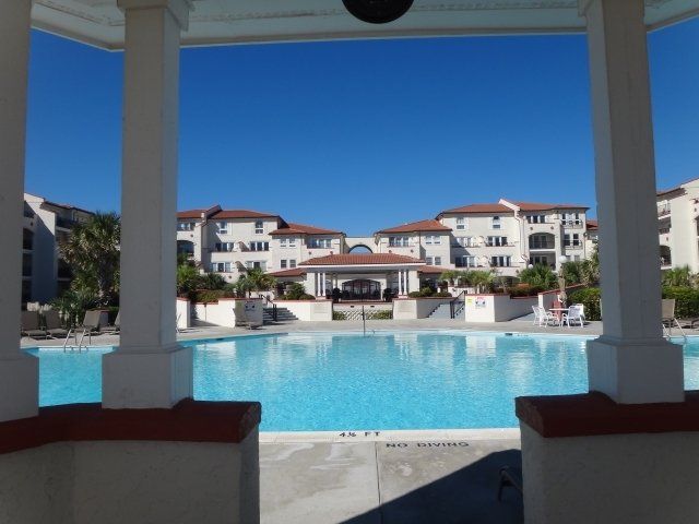 A gazebo overlooking a large swimming pool with a building in the background