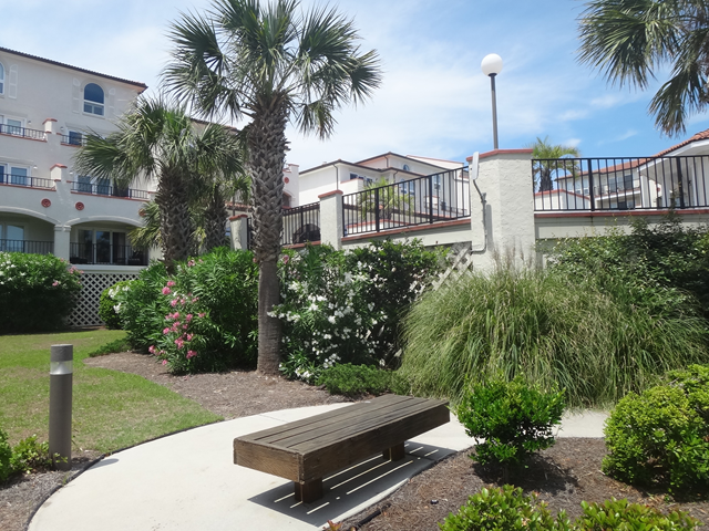 A wooden bench sits in the middle of a garden in front of a building