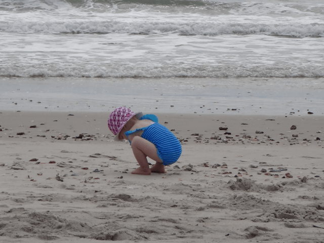 A little girl in a blue bathing suit is kneeling on the beach