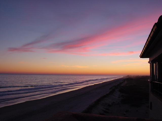 A sunset over the ocean with a house in the foreground