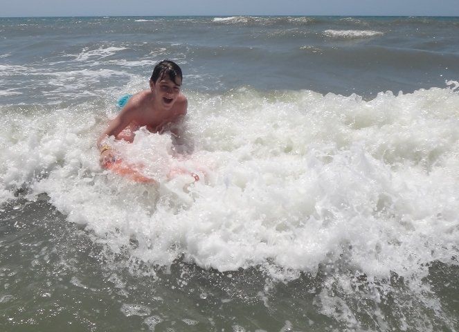 A young boy is riding a wave on a boogie board in the ocean.