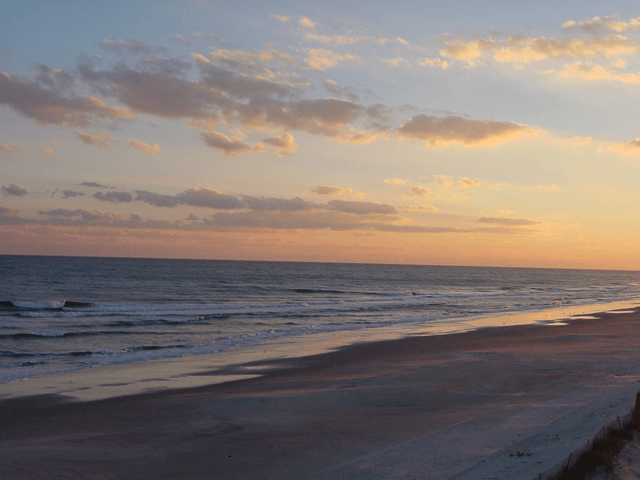 A beach at sunset with a few clouds in the sky