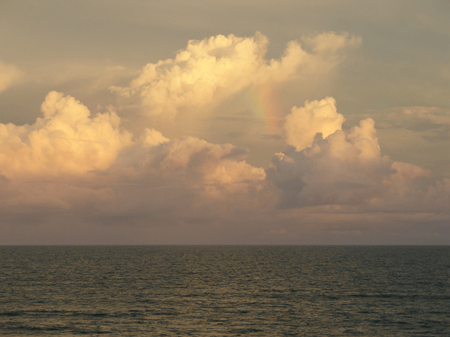 A rainbow is visible in the clouds over the ocean