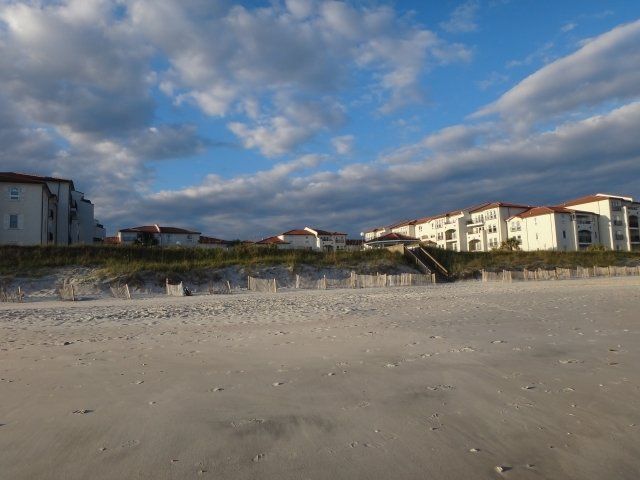 A beach with buildings in the background and a blue sky with clouds