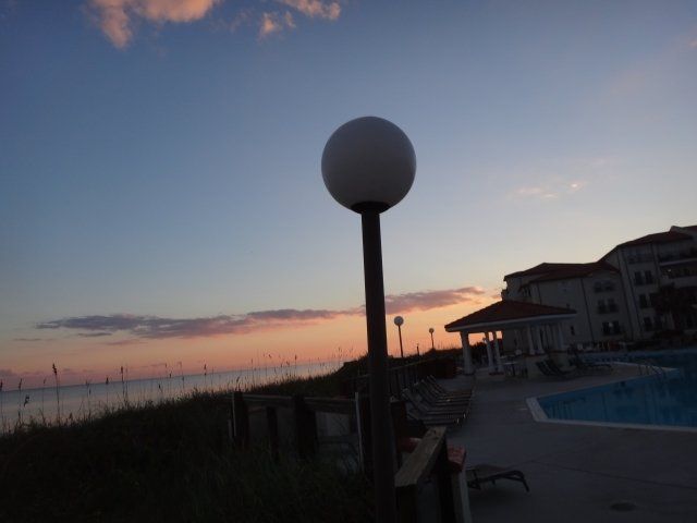 A sunset over a swimming pool with a lamp post in the foreground