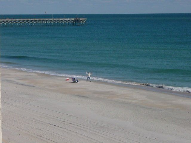A beach with a pier in the background and a person standing on the beach