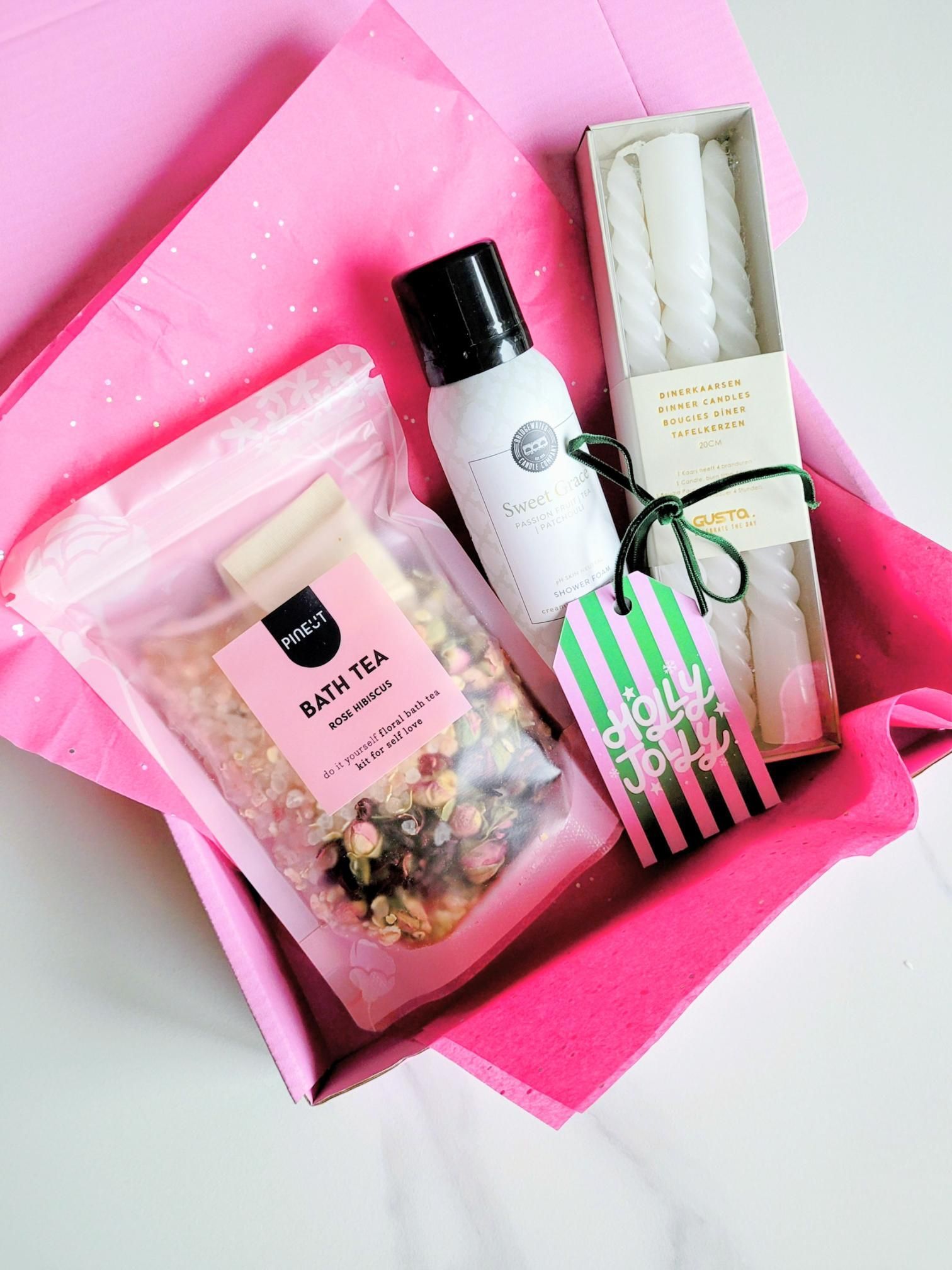 Roze geschenkdoos met badthee, kaarsen en een plantenspuit op roze vloeipapier.