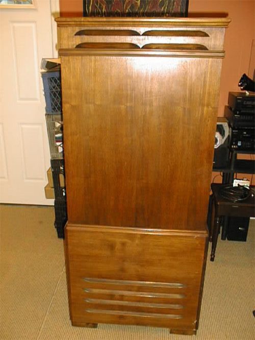Tall wooden cabinet with ventilation slats at bottom, in front of a white door.